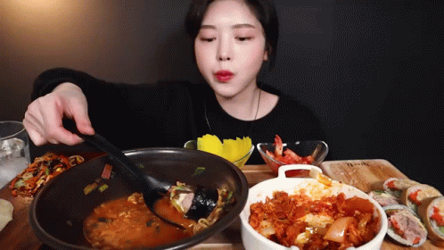 A Woman Is Sitting At A Table Eating A Bowl Of Food GIF