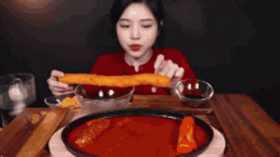 A Woman Is Sitting At A Table Eating A Large Piece Of Food GIF