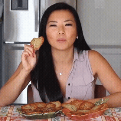 A Woman Is Sitting At A Table Eating A Piece Of Food GIF
