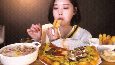 A Woman Is Sitting At A Table Eating A Pizza And French Fries GIF