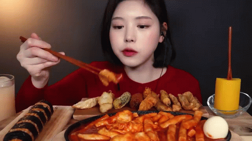 A Woman Is Sitting At A Table Eating A Variety Of Foods With Chopsticks . GIF