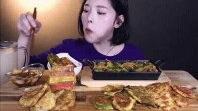 A Woman Is Sitting At A Table Eating Food From A Pan GIF