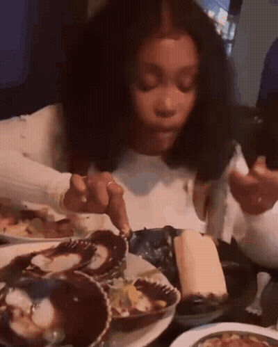 A Woman Is Sitting At A Table Eating Oysters With A Fork . GIF