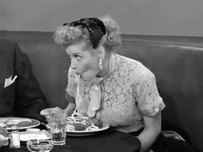A Woman Is Sitting At A Table Eating Spaghetti With A Spoon GIF