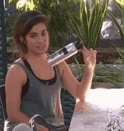 A Woman Is Sitting At A Table Holding A Bottle On Her Shoulder That Says ' Stainless Steel ' On It GIF