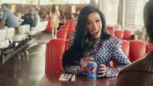 A Woman Is Sitting At A Table Holding A Can Of Pepsi . GIF