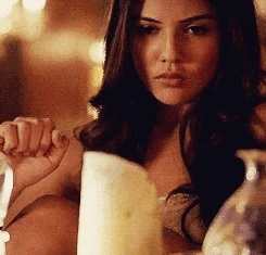A Woman Is Sitting At A Table Holding A Candle . GIF