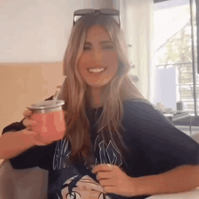 A Woman Is Sitting At A Table Holding A Pink Cup . GIF