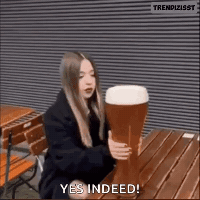 A Woman Is Sitting At A Table Holding A Very Large Glass Of Beer . GIF