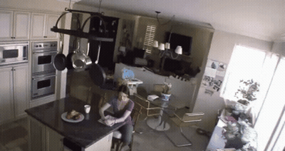A Woman Is Sitting At A Table In A Kitchen Reading A Book GIF