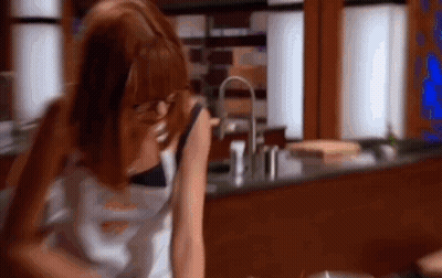 A Woman Is Sitting At A Table In A Kitchen Talking On A Phone . GIF