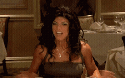 A Woman Is Sitting At A Table In A Restaurant Holding A Glass Of Liquid . GIF