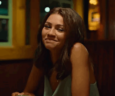 A Woman Is Sitting At A Table In A Restaurant Smiling At The Camera . GIF