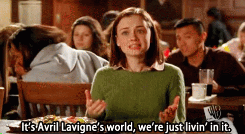 A Woman Is Sitting At A Table In A Restaurant Talking About Avril Lavigne 'S World GIF