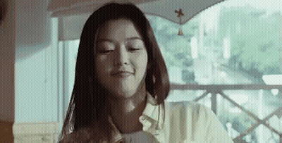 A Woman Is Sitting At A Table In Front Of A Window And Smiling . GIF