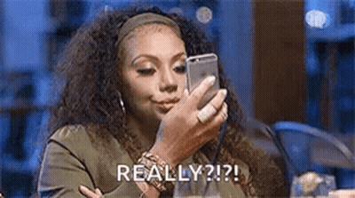 A Woman Is Sitting At A Table Looking At A Cell Phone . GIF