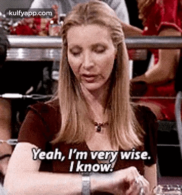A Woman Is Sitting At A Table Looking At Her Watch And Saying Yeah , I 'M Very Wise . GIF
