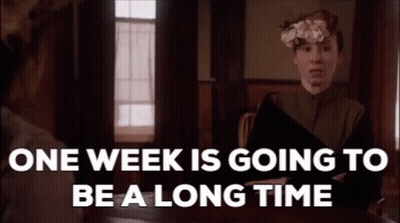 A Woman Is Sitting At A Table With A Book In Her Hand And A Flower In Her Hair While Talking To Another Woman . GIF