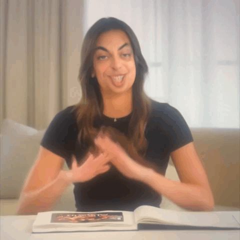 A Woman Is Sitting At A Table With A Book On It GIF