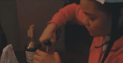 A Woman Is Sitting At A Table With A Bottle Of Wine In Her Hands . GIF