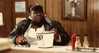 A Woman Is Sitting At A Table With A Bucket Of Town Chicken In Front Of Her GIF
