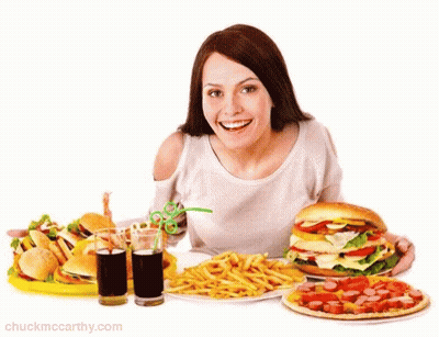 A Woman Is Sitting At A Table With A Bunch Of Food Including A Hamburger French Fries And A Pizza GIF