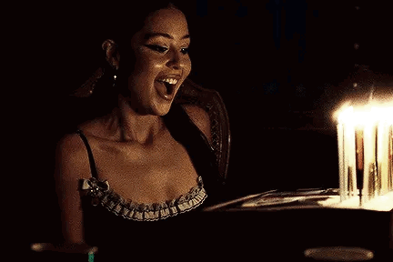 A Woman Is Sitting At A Table With A Cake And Candles . GIF