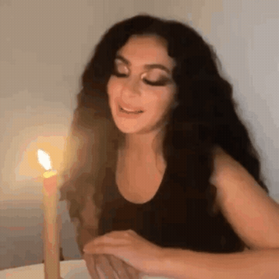 A Woman Is Sitting At A Table With A Candle In Front Of Her . GIF