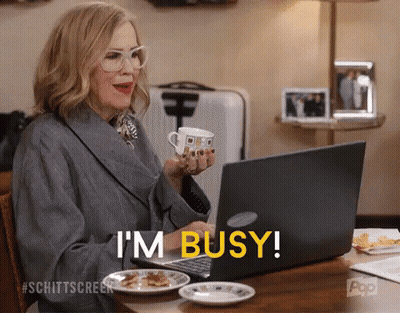 A Woman Is Sitting At A Table With A Cup Of Coffee And A Laptop And Says I 'M Busy GIF