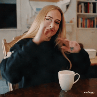 A Woman Is Sitting At A Table With A Cup Of Coffee And The Name Adelaide Is On The Bottom GIF