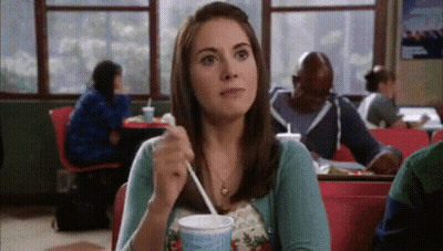 A Woman Is Sitting At A Table With A Cup Of Milkshake GIF
