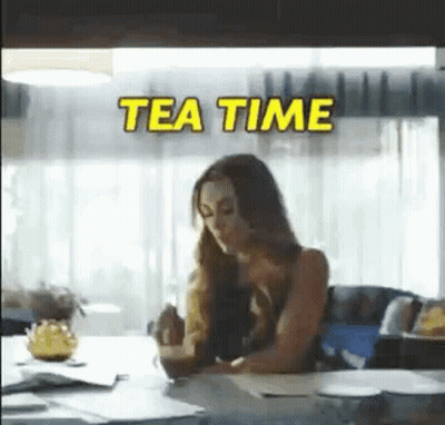 A Woman Is Sitting At A Table With A Cup Of Tea In Her Hand . GIF