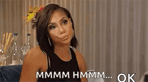 A Woman Is Sitting At A Table With A Flower In Her Hair And Making A Face . GIF