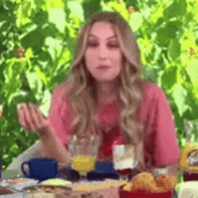 A Woman Is Sitting At A Table With A Glass Of Orange Juice And A Plate Of Food . GIF