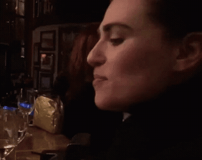 A Woman Is Sitting At A Table With A Glass Of Water In Front Of Her GIF