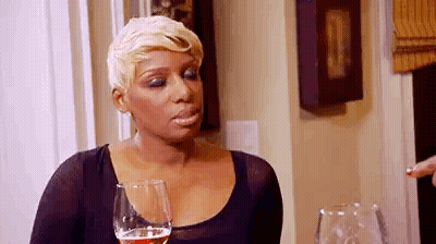 A Woman Is Sitting At A Table With A Glass Of Wine And Making A Funny Face . GIF