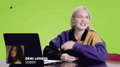 A Woman Is Sitting At A Table With A Laptop And A Picture Of Demi Lovato . GIF