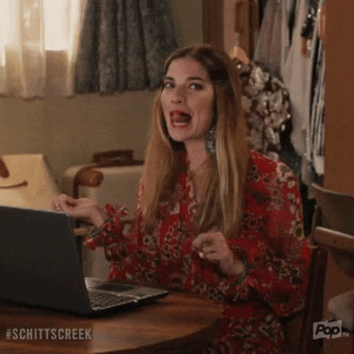 A Woman Is Sitting At A Table With A Laptop Computer And Making A Funny Face . GIF