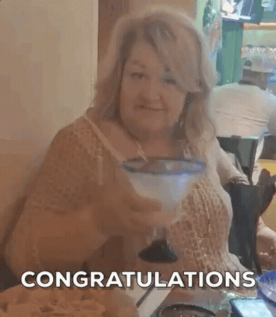 A Woman Is Sitting At A Table With A Margarita In Her Hand And The Words `` Congratulations '' Behind Her . GIF