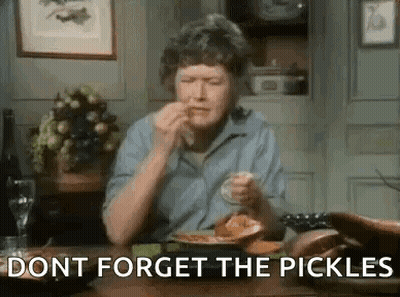 A Woman Is Sitting At A Table With A Plate Of Food And Pickles . GIF