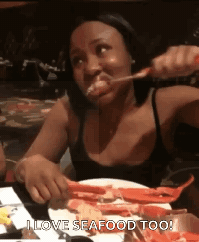 A Woman Is Sitting At A Table With A Plate Of Seafood And Eating It . GIF