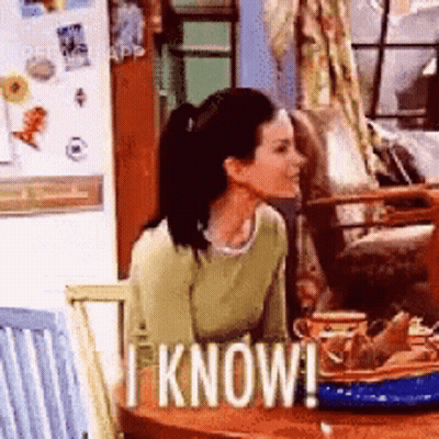 A Woman Is Sitting At A Table With A Sign That Says I Know ! GIF