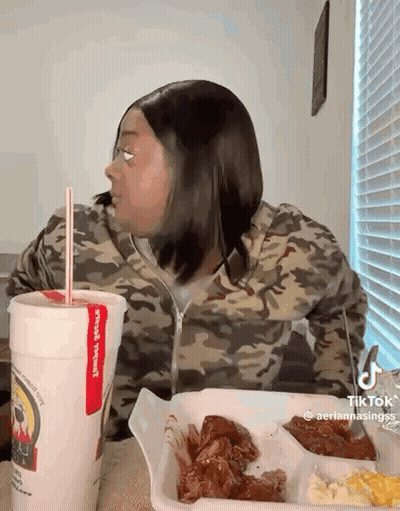 A Woman Is Sitting At A Table With A Tray Of Food And A Drink . GIF