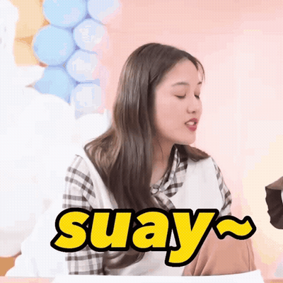A Woman Is Sitting At A Table With Balloons In The Background And The Word Suay In Yellow Letters GIF