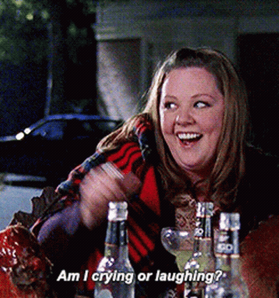 A Woman Is Sitting At A Table With Bottles Of Liquor And Says Am I Crying Or Laughing GIF