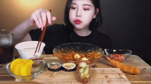 A Woman Is Sitting At A Table With Chopsticks Eating Food GIF