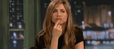 A Woman Is Sitting At A Table With Her Finger On Her Chin And Making A Funny Face . GIF