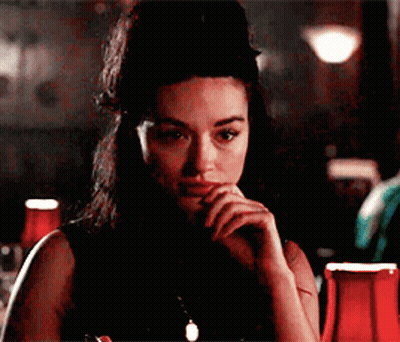 A Woman Is Sitting At A Table With Her Hand On Her Face GIF