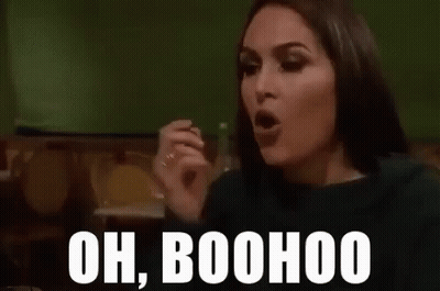 A Woman Is Sitting At A Table With Her Hand Up And The Words `` Oh Boohoo '' Written On Her Face . GIF