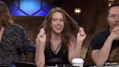 A Woman Is Sitting At A Table With Her Hands In Her Hair While A Man Looks On . GIF